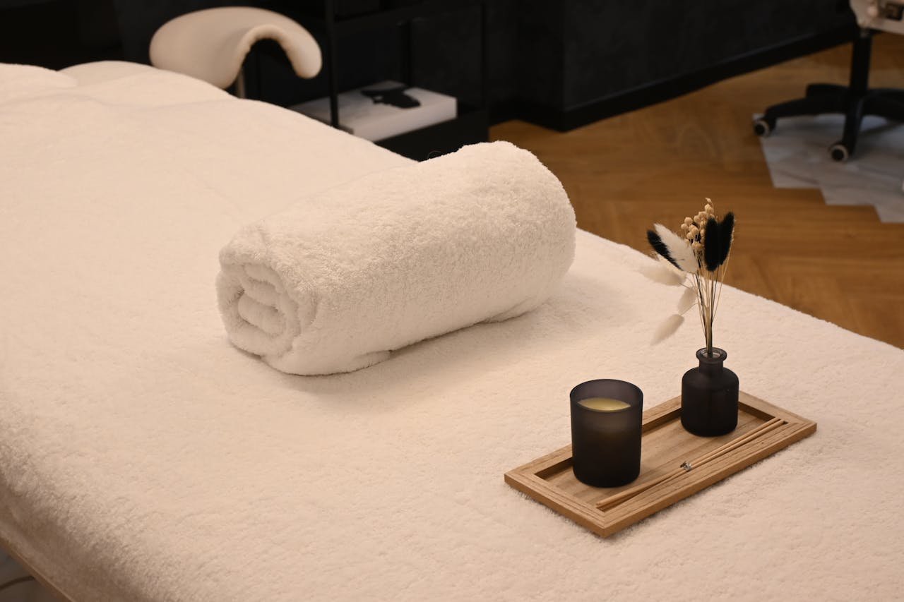A serene spa massage table setup with a rolled towel, candle, and decorative vases in a relaxing environment.